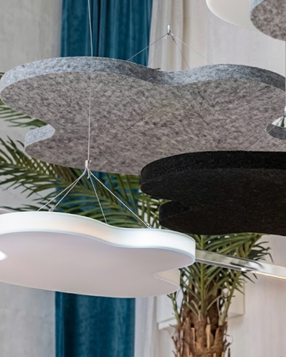 Cloud-shaped suspended acoustic felt ceiling panels in gray, black, and white, hanging in a modern interior space with a plant and blue curtains in the background.