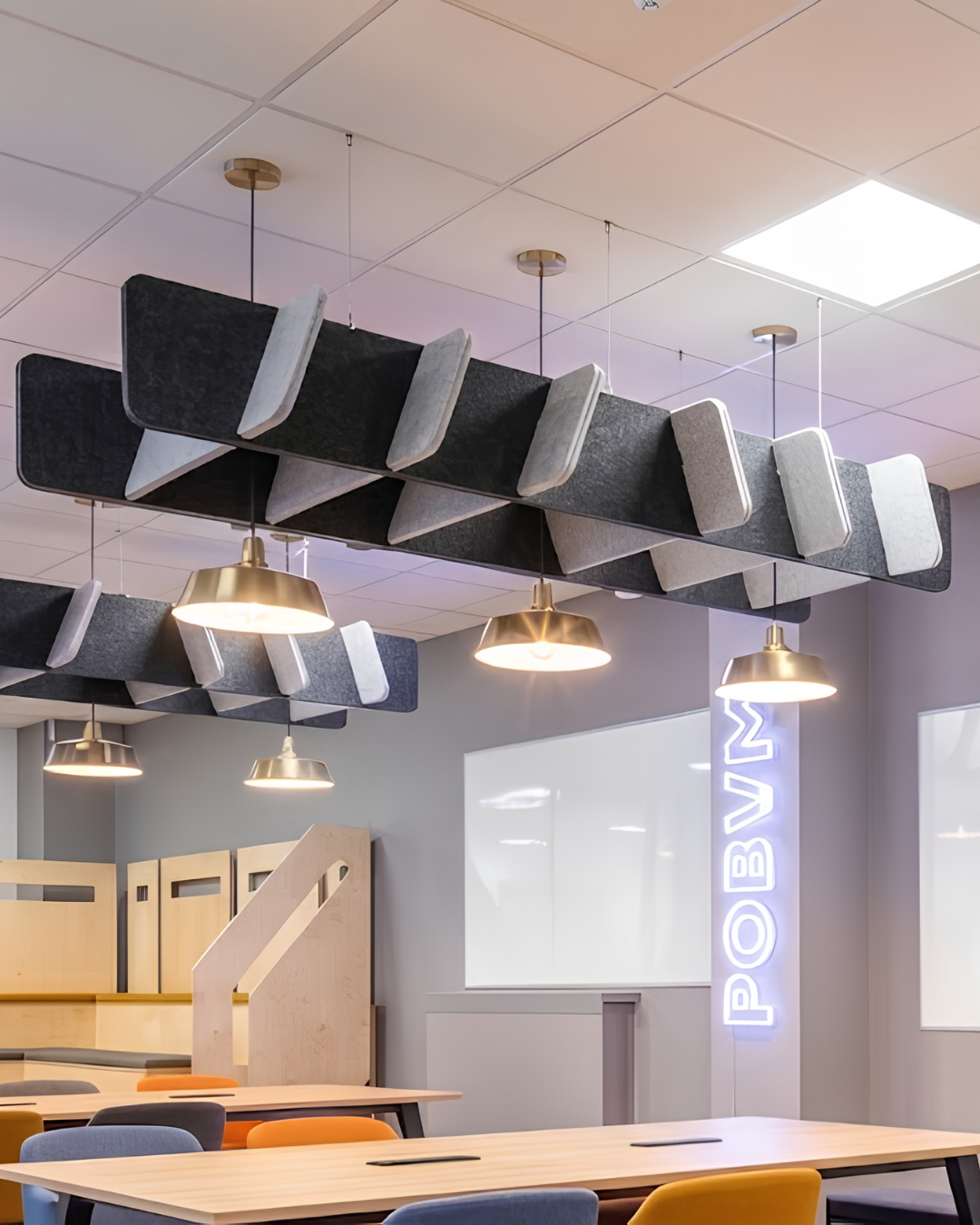 Acoustic Baffle ceiling panels suspended in a classroom or conference space, with pendant lights, wooden tables, chairs, and a whiteboard in the background.