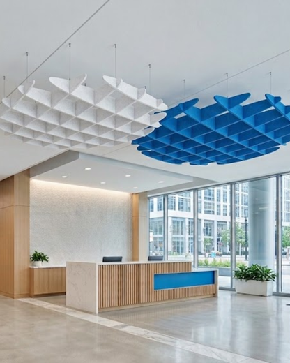 Modern office lobby interior with a reception desk, large glass windows, and two large Acoustic Baffle ceiling panels light fixtures in white and blue suspended from the ceiling.