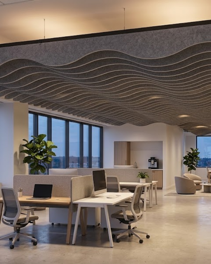 A modern open office space with a large wavy Acoustic Baffle ceiling panels, white desks, gray office chairs, and large windows looking out onto a city view at dusk.